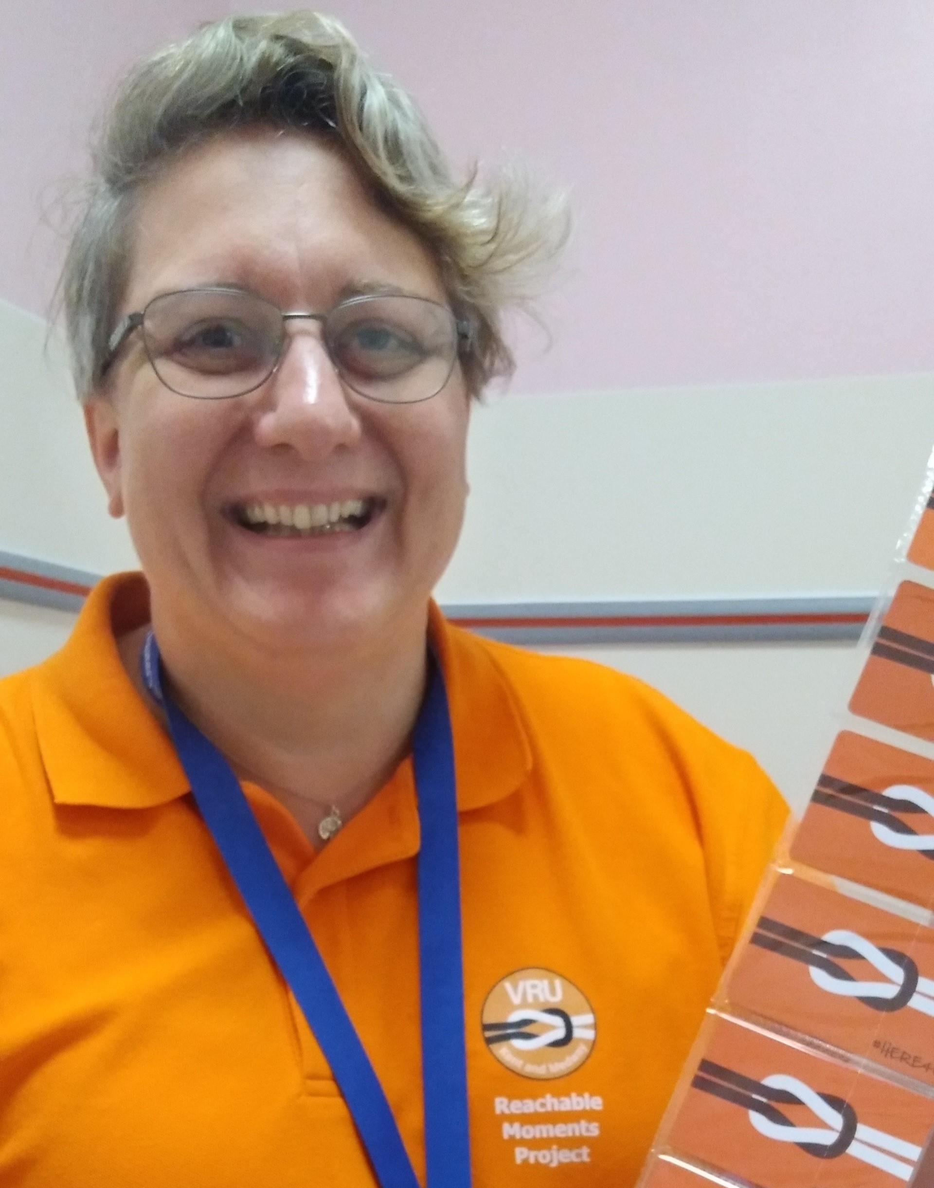 Picture showing Stacey Gibson who is a Reachable Moments worker at Ashford Hospital. Stacey is wearing a VRU branded t-shirt in orange and is facing the camera.